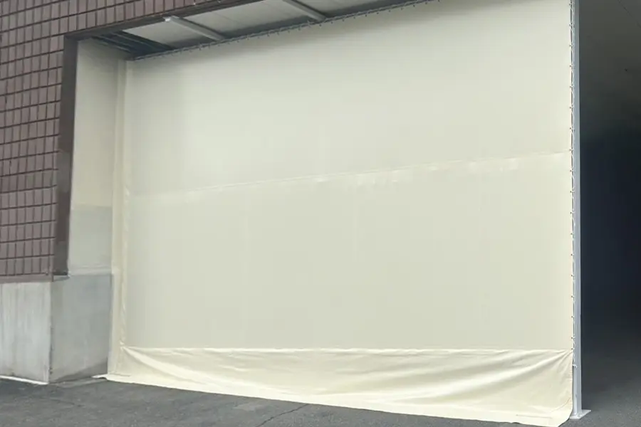 工場のシャッター開口部に設置された遮熱効果のあるアイボリー色のビニールカーテン