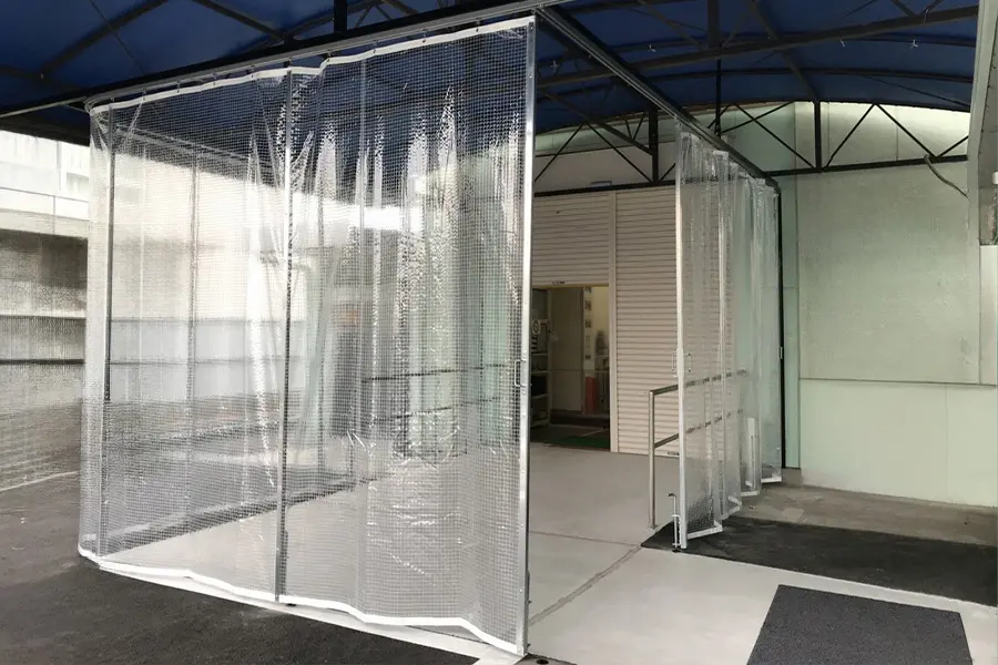 デルマシリーズ屋外用設置事例 - 屋根付き通路の開口部に設置された屋外用ビニールカーテンによる間仕切り効果